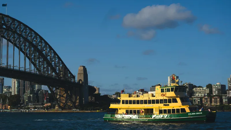 A green and yellow Sydney ferry crossing the harbour with the Sydney Harbour Bridge behind it